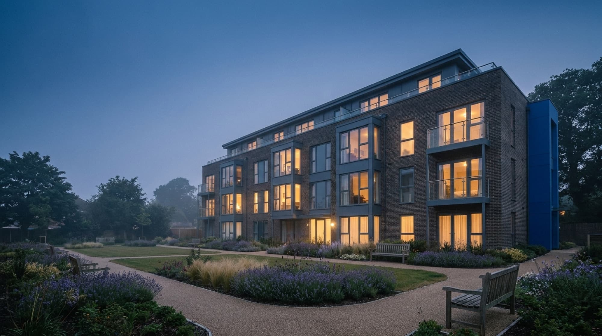 A self-managing residential block at dusk — warm-lit homes above landscaped gardens